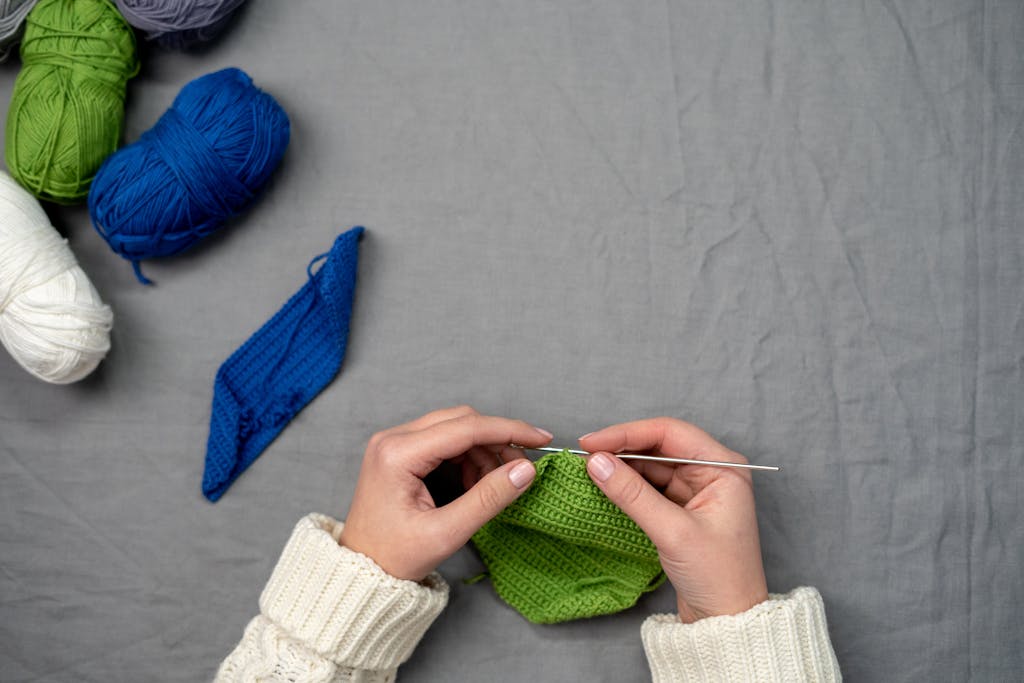 Hands knitting with vibrant yarn on a grey backdrop, showcasing creativity and leisure activity.